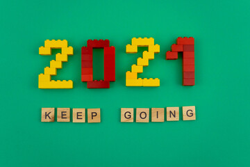 The words keep going 2021 is lined with wooden letters on a green background. Figures from the constructor top view. Postcard in place for text. Flatlay. Yellow and red numbers. Copy space.