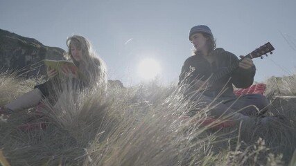 Guy And Girl Sitting In Field Playing Small Guitar And Reading Bible