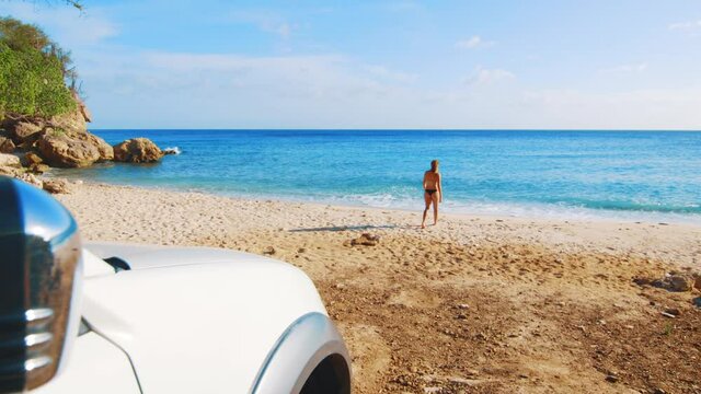 Car in the foreground with a girl walking in bikini towards the beach in the background