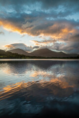 Naklejka na ściany i meble Beautiful sunrise landscape image looking across Loweswater in the Lake District towards Low Fell and Grasmere with vibrant sunrise sky breaking on the mountain peaks