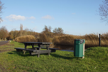 Wooden bench and table in the grass along a road and a ditch with reed in the autumn near the Dutch...