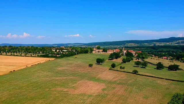 upwards moving drone shot of small village in the distance, Taize, France. The village is on the hill, green and yellow around.