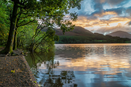 Beautiful sunrise landscape image looking across Loweswater in the Lake District towards Low Fell and Grasmere with vibrant sunrise sky breaking on the mountain peaks