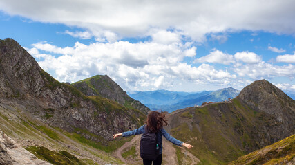 Naklejka premium Young female tourist on the background of a mountain panorama. Standing with arms outstretched,