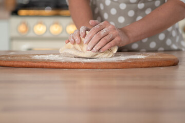 Fototapeta na wymiar Knead dough, hand dough and flour close-up. A pastry chef in a grey polka-dot apron.