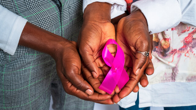 close up image of two black people hands holding a pink ribbon -concept on African breast cancer awareness month