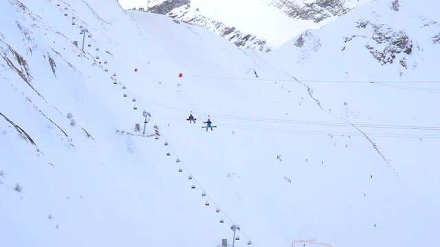 Snowboarders ride a zip line by aerial cableway, descend from the mountain to the base. Winter ski resort. Entertainment, recreation, vacation. Slow motion video