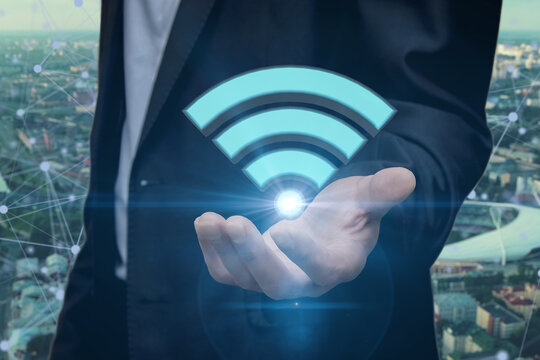 A businessman holds a shining Wi-Fi icon against the city background. Concept: free Internet connection, unlimited traffic, network and communications.