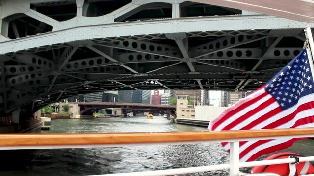 Under a bridge off the back of a ferry on the Chicago River watching an American flag wave and water taxi pass.