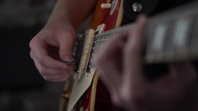 Man goes from strumming chords to picking individual notes on a Les Paul style guitar - close up side shot of his strumming hand