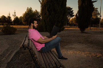 Caucasian man reading a book in the park while wearing a pink shirt and jeans