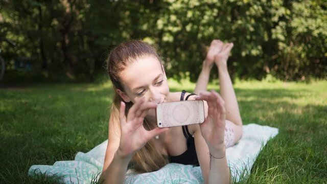 Beautiful caucasian woman laying in a grassy field taking a picture with her smart phone.