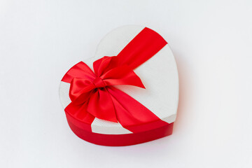gift in white box in shape of  heart with a red ribbon bow isolated on white background. composition for Valentine day, birthday, mother day or christmas.  copyspace.  angle view.