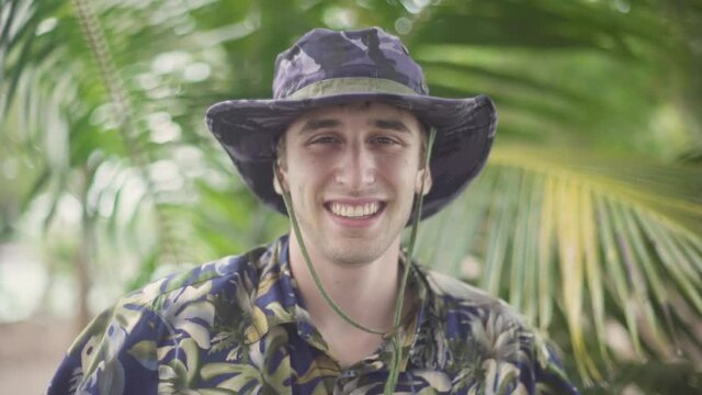 Young male explorer in Hawaiian shirt and Wide Brim Hat smiles into the camera. Portrait in tropicals setting