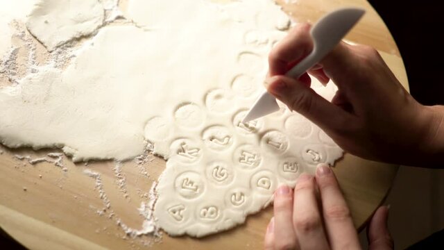 From above look of Confectioner woman hands cutting letters out of sugar marzipan fondant icing