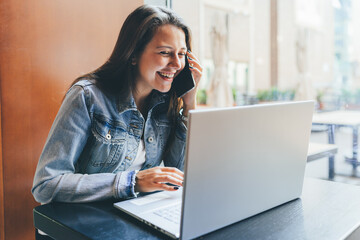 Young smiling woman at cafe work on laptop computer and talk by phone.