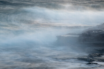 Rocky seashore with wavy ocean and waves crashing on the rocks.