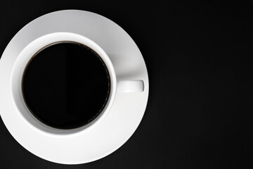 A white Cup full of black coffee stands on a saucer on the left on a black background