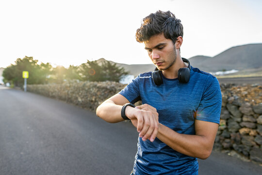 Joven corriendo por la carretera con auriculares y reloj inteligente deportivo