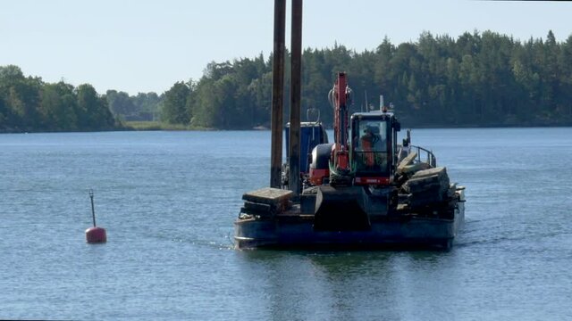 An excavator on a scow heading towards the marina