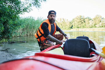 Close up shot man sitting near canoe on sandy beach