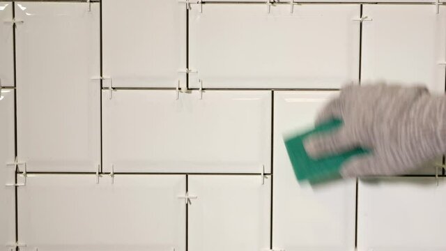 Working tiler laying white ceramic tile in a herringbone pattern on wall in kitchen.