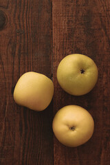 Three ripe fresh yellow apples lying on a wooden table. Natural wood texture. Top view.
