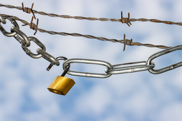 Fototapeta na wymiar Padlock and steel chains with barbed wire against blue clouded sky symbolizing lockdown