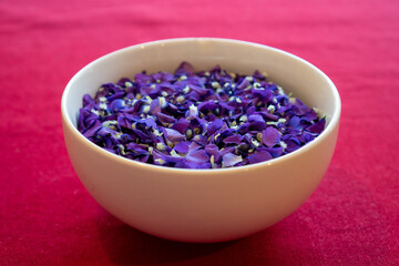 Obraz na płótnie Canvas White bowl filled with picked violet flowers on red tablecloth