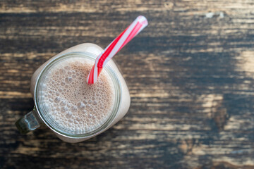 Glass mug of chocolate milkshake on wooden background. Top view, copy space