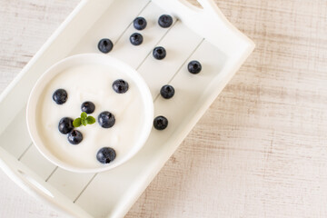 Bowl with yogurt and blueberries on an white wooden tray, top view