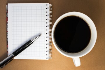On a brown background a Notepad with a blank sheet next to which is a white Cup of black coffee