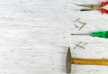 Hand tools on a white wooden background, hammer with nails and a screwdriver with different screws...