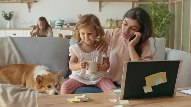 A Busy Mother Trying to Work Remotely With Her Children's at Home. The Daughter Interferes With Her Mother's Work. A Little Daughter Don't Want to Sits on the Lap of Her Mother. Mother Begin Annoyed.