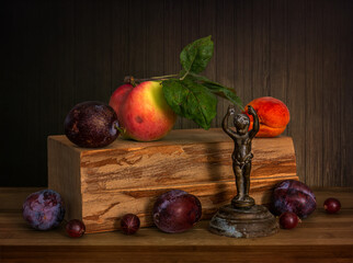 Ripe and beautiful apple with green leaves, plum and apricot on a wooden block. Gooseberries and an old bronze figurine. Still life. Vintage.