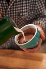 Man's hands pouring a milk into cacao