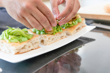 Traditional Italian cuisine: chef prepares slices of white pizza with mozzarella, vegetables, walnuts, ham, courgettes, basil, on a designer plate, for quality cuisine. food photography 