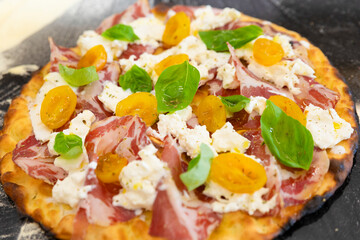 Italian cuisine: preparation of white pizza, with yellow tomatoes, white mozzarella, red ham and green basil. Design serving. professional cook at work. food photography for menus and websites