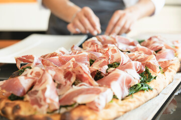 Italian cuisine: preparation of white pizza, with red ham, white mozzarella and green vegetables. Design serving. professional cook at work. food photography for menus and websites