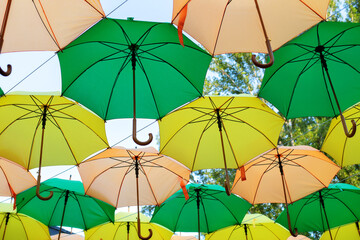 Green and yellow umbrellas hanging above city streets. Colorful umbrellas in sky. Street decoration. Street with colorful umbrellas. Sun umbrellas against blue sky. Rainy weather umbrella. Rain. Storm