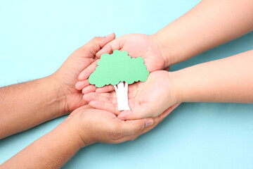 hands holding paper tree  on blue background.