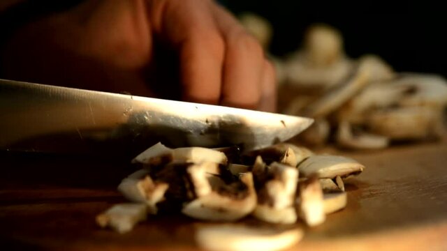 Cutting champignons on a wooden breadboard with an iron knife.