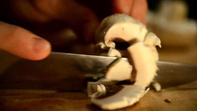Cutting champignons on a wooden breadboard with an iron knife.