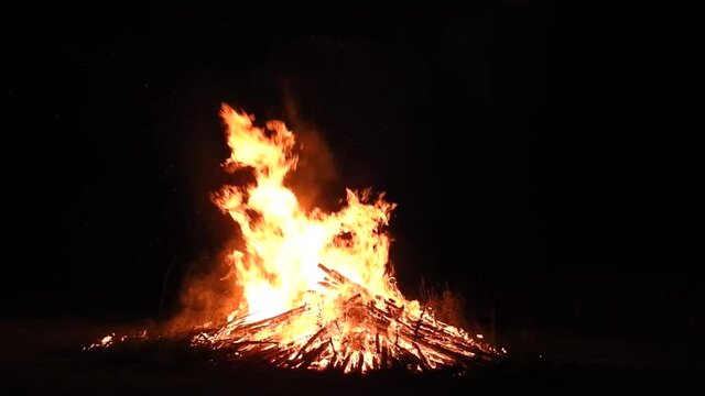 Huge solstice campfire burning in the black of night. Wideshot.