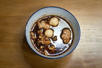 Traditional Thai style tomyum (spicy) pork noodle is served in bowl, placed on wooden table. Selective focus on the part of meat ball and sliced pork.