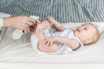 Mother puts socks on the baby. The baby is lying on the changing table and smiling