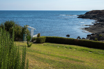 Beautiful azure blue Black Sea with stony black shore and summer green meadow and rosemary in the...