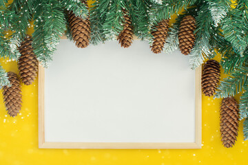 on a yellow background - a wooden photo frame, decorated on top with fir branches with cones. The...