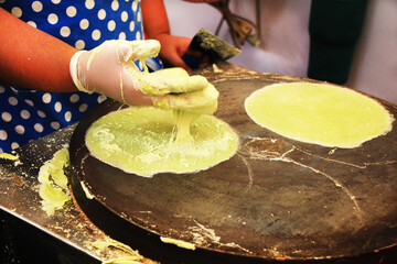 The hand man is making roti by applying the kneaded flour onto the pan and making a sheet for eating.