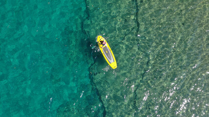 Aerial drone top down photo of unidentified woman exercising in SUP or Stand Up Paddle board in exotic island emerald beach